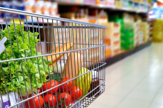 Shopping cart full of food in the supermarket aisle. Side tilt view. Horizontal composition